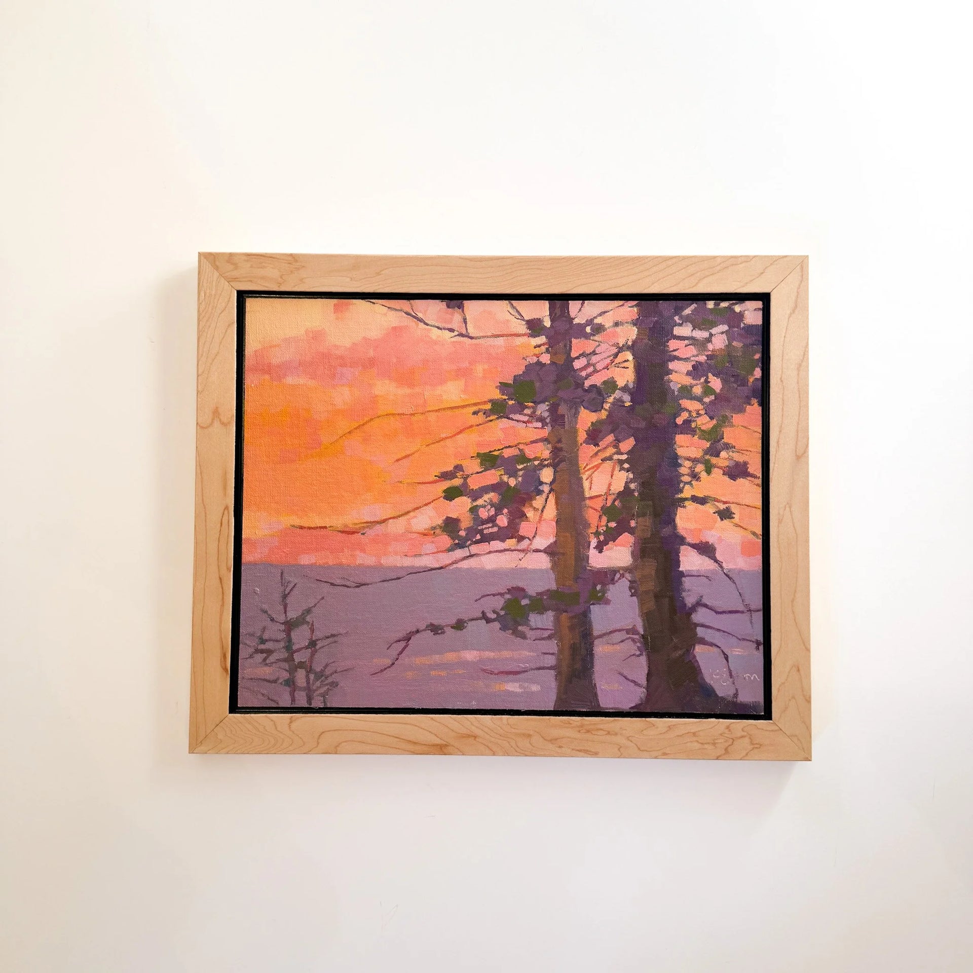 Framed artwork of trees against a sunset sky on a beige wall