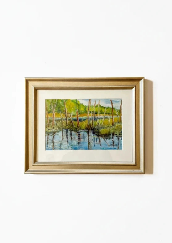 Framed painting of a landscape with trees and water on a white background