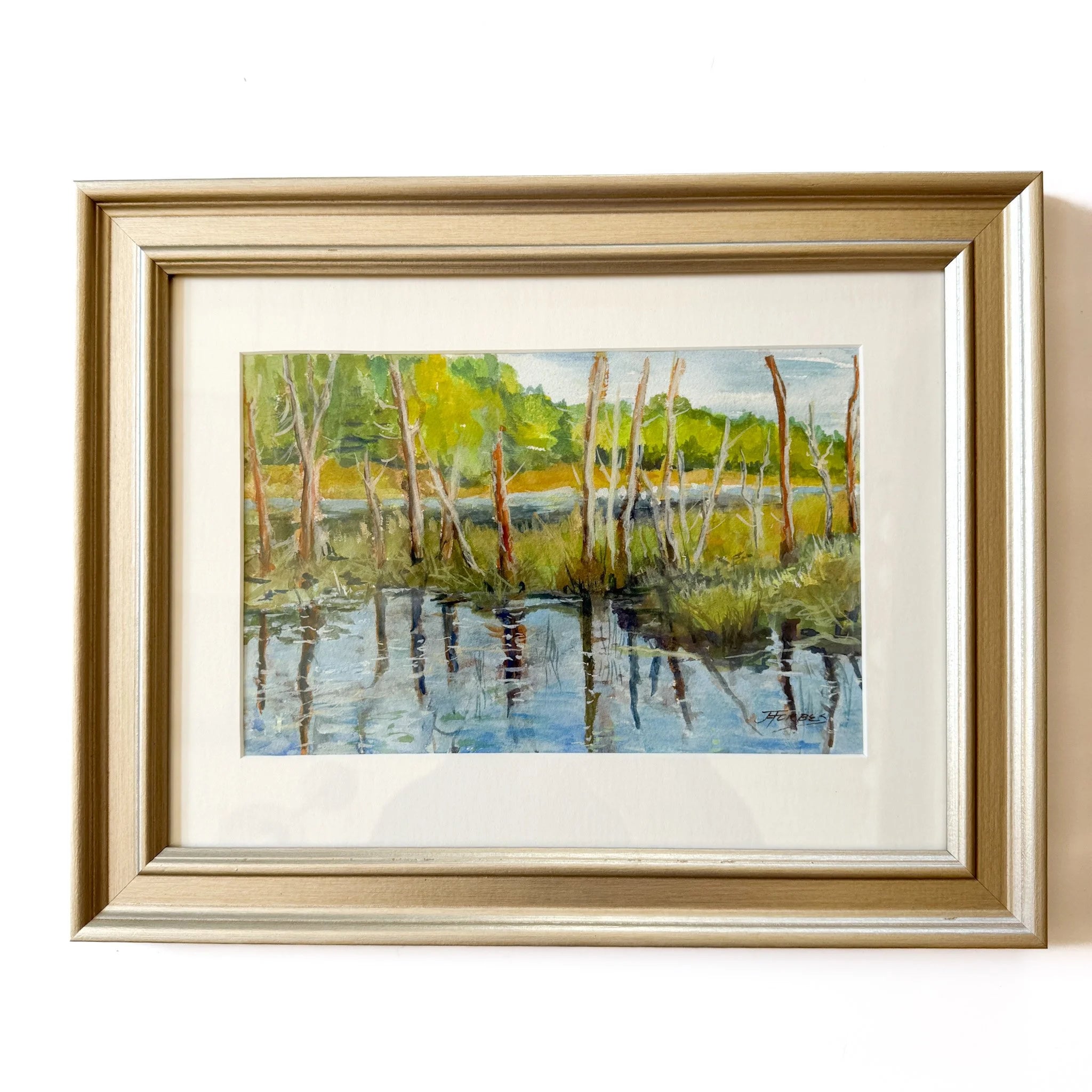 Framed painting of a landscape with trees and water.