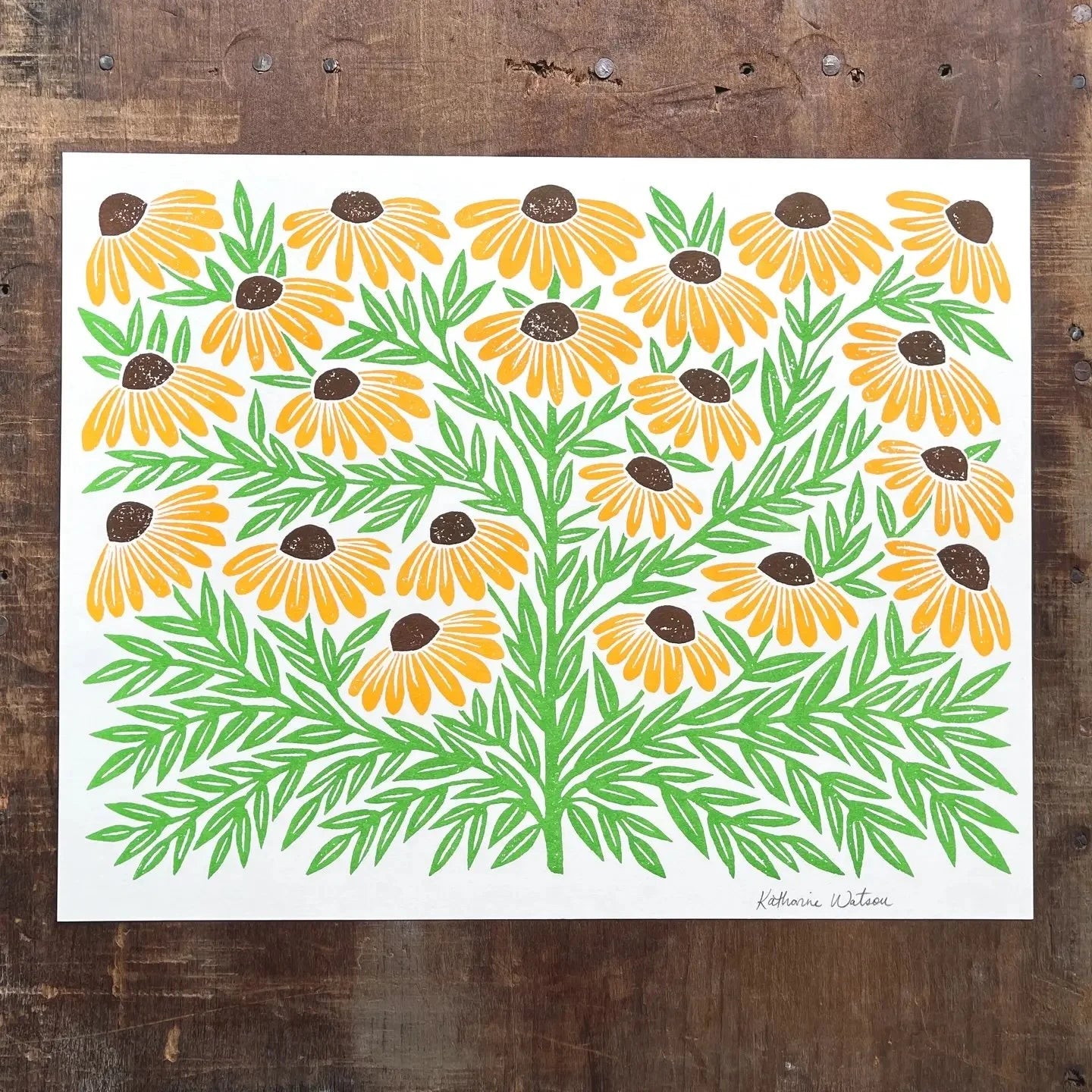 Art print with yellow and orange flowers on a white background, placed on a wooden surface.